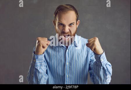 Angry frustrated aggressive man clenching fists and screaming isolated on gray background Stock Photo