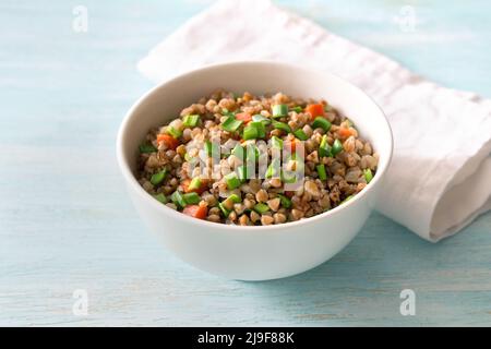 Delicious vegan buckwheat with vegetables and green onions on a light blue wooden background. Healthy homemade food Stock Photo