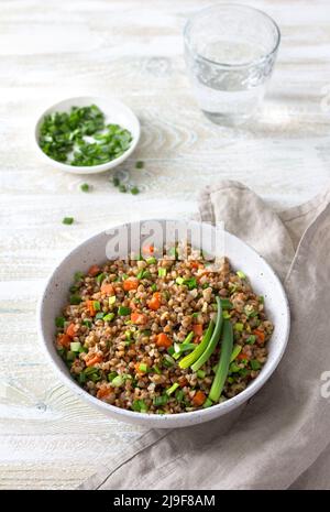 Delicious vegan buckwheat with vegetables and green onions on a light wooden background. Healthy homemade food Stock Photo