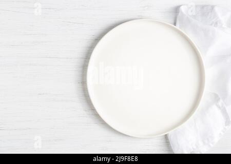 White empty plate and on linen napkin on white wooden table. Stock Photo