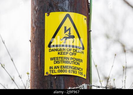 A yellow triangle Danger of Death, Keep Off electricity sign (Western Power Distribution) isolated outdoors on a post in UK countryside. Stock Photo