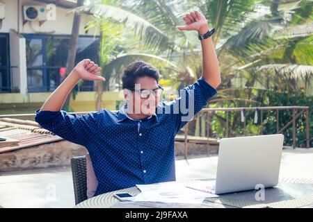 handsome and successful indian man in a stylish well-dressed freelancer working with a laptop on the beach.freelance and remote work.businessman Stock Photo