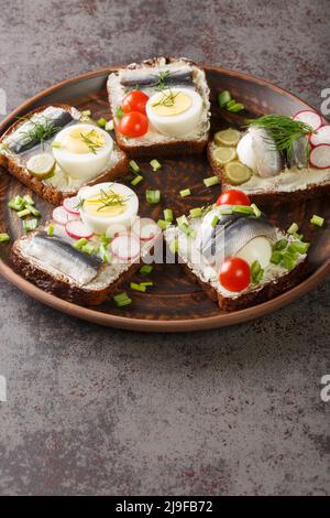 Sandwich with sprat fillet, eggs, various vegetables close-up in a plate on the table. Vertical Stock Photo