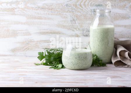 Healthy dietary green kefir (yogurt) with herbs in glass and bottle on wooden table, space, selective focus Stock Photo