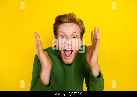 Photo of funky impressed guy dressed green sweater open mouth rising arms isolated yellow color background Stock Photo