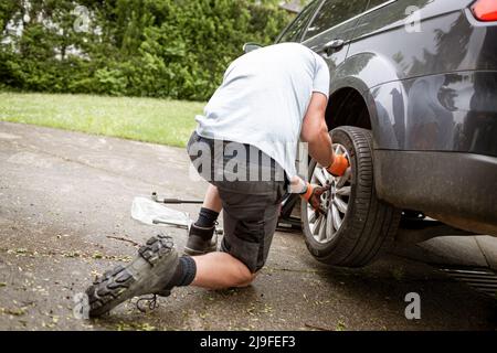Middle aged man with grey hair changes tires on his family car van Stock Photo