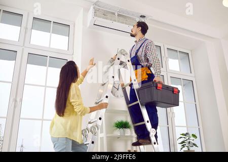 Repairman repairs air conditioner and cleans air filter on indoor unit at client's home. Stock Photo