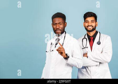 portrait of smiling medical worker in white lab coat with stethoscope conferring with young doctor on blue background Stock Photo