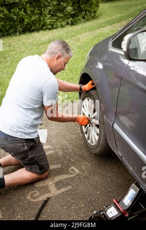 Middle aged man with grey hair changes tires on his family car van Stock Photo