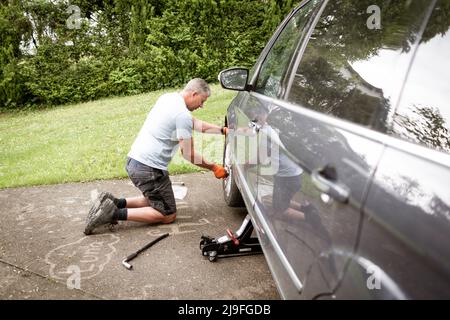 Middle aged man with grey hair changes tires on his family car van Stock Photo