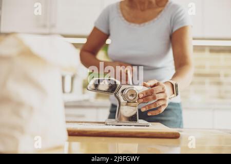 A woman standing in the kitchen at the table cuts noodles in a noodle cutter Stock Photo
