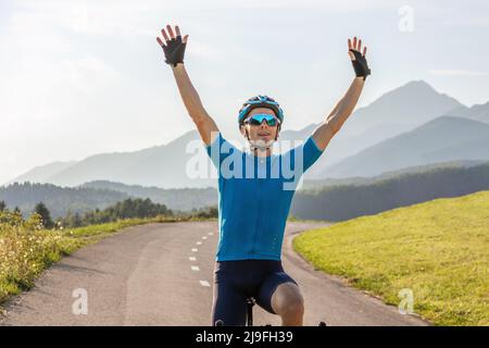 Male athlete professional racing cyclist riding a bike with arms raised above the head, in a victory pose Stock Photo