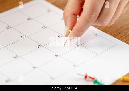 Hands fixing notes schedule, white pin thumbnail in calendar for  meeting and appointment reminder Stock Photo