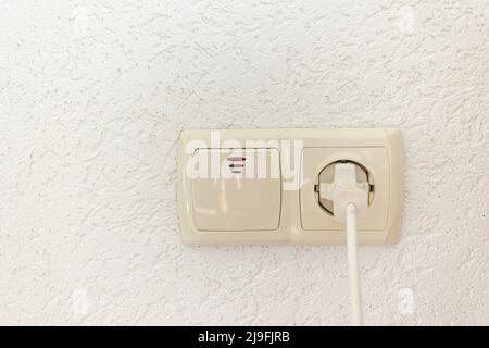 white socket with plug and light switch on an empty wall Stock Photo
