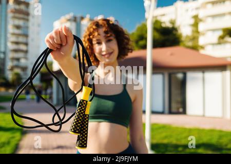 Young happy redhead woman wearing green sports bra on standing city park,  outdoors holding her skipping rope in front of the camera. Outdoor sport,  he Stock Photo - Alamy