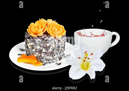 A small cake with candied orange and chocolate chips, a cup of tea and a flower on a black background. Selective focus Stock Photo
