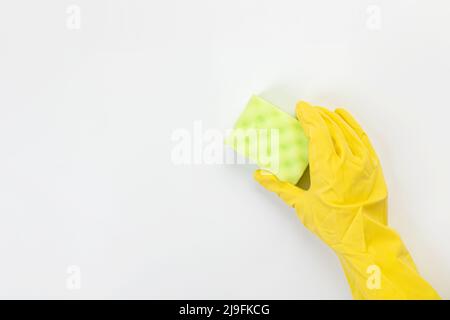 The hand of a housewife in a yellow protective rubber glove holds a sponge for cleaning agent on a gray background. Detergent for various surfaces in Stock Photo
