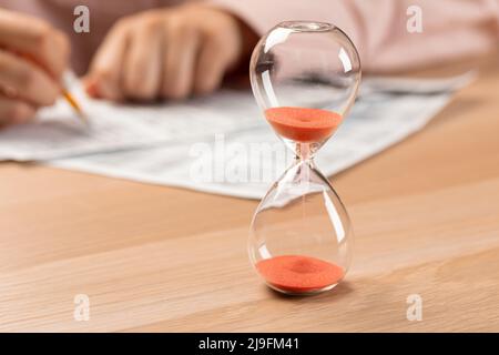 Hourglass with time running out and student hand testing in exercise and passing exam carbon paper computer sheet with pencil in school test room Stock Photo