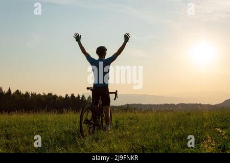 Male athlete professional racing cyclist riding a bike with arms raised above the head, in a victory pose Stock Photo