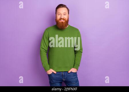 Photo of attractive foxy male holding hands in pockets posing on camera wear green pullover isolated on violet color background Stock Photo