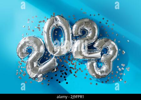 Silver numbers 2023 new year balloons among confetti in sunlight on blue background Happy new year celebration party. Greetings and congratulation Stock Photo