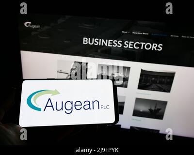 Person holding cellphone with logo of British waste management company Augean plc on screen in front of business webpage. Focus on phone display. Stock Photo