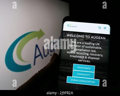 Person holding smartphone with website of British waste management company Augean plc on screen with logo. Focus on center of phone display. Stock Photo