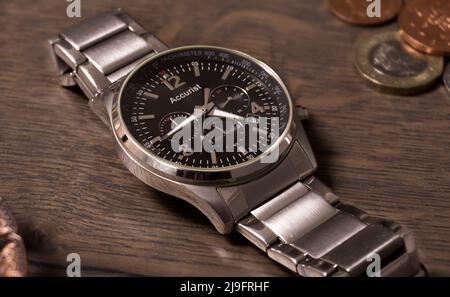Side profile of a silver analogue watch on a wooden table with coins Stock Photo