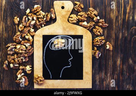 drawn person head with brain and nuts walnuts on wooden background. Concept of healthy food for a human to think. Stock Photo
