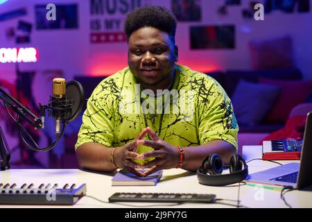 Stylish young Black man wearing neon yellow T-shirt sitting in at desk in amateur broadcasting studio Stock Photo