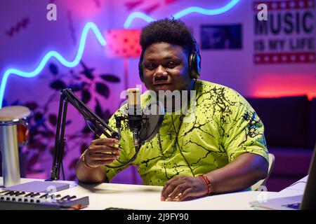Young African American man wearing headphones adjusting microphone to start podcast or broadcast recording in home studio Stock Photo