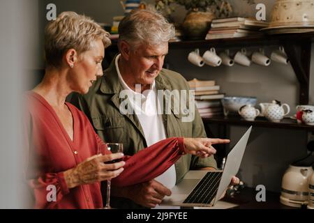 caucasian mature couple reading off laptop while cooking in kitchen Stock Photo