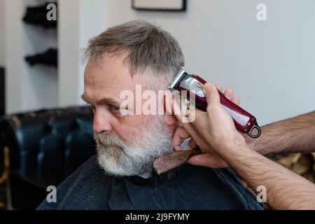 An old man enjoing haircut by a master in a barbershop.  An old man gets a stylish haircut Stock Photo
