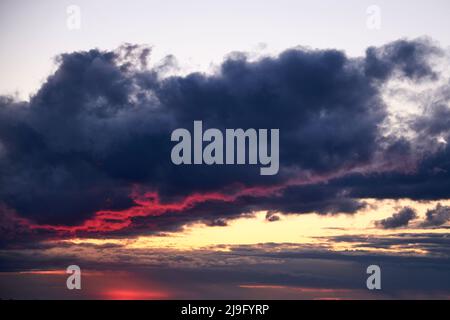 A large rain cloud with a reflection of light from the red sun at sunrise Stock Photo