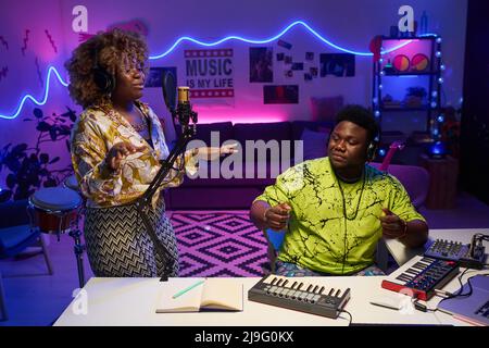 Modern gen Z African American man and woman wearing stylish casual outfits enjoying working together on song in home recording studio Stock Photo