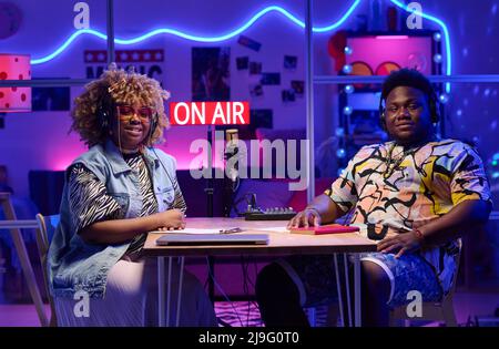 Portrait of modern young gen Z African American influencers sitting at desk in broadcasting studio at home looking at camera Stock Photo