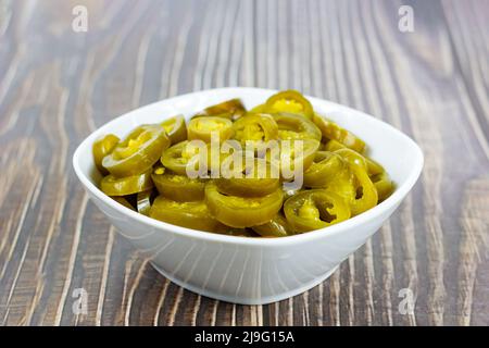 Green spicy sliced marinated jalapeno pepper in white bowl on light background in the kitchen. Stock Photo