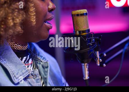 Side view close-up of young Black woman sitting in front of microphone recording podcast or doing radio broadcasting Stock Photo