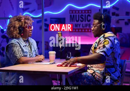 Young gen Z African American man and woman sitting in front of each other recording podcast or doing radio broadcasting in studio at home Stock Photo