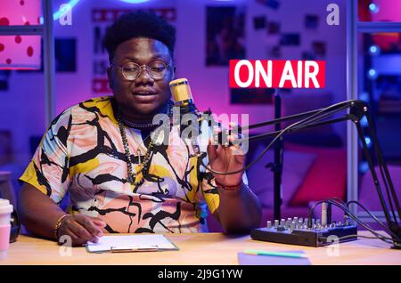 Horizontal medium portrait of handsome young African American influencer wearing stylish casual clothes recording podcast speaking on topic Stock Photo