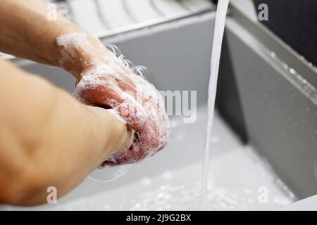 A man washes his hands with soap under the tap under running water close-up. Health, cleanliness and hygiene concept. Stock Photo