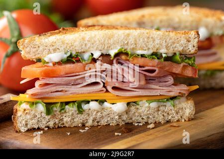 Closeup of ham sandwich with cheese, lettuce and tomato on whole grain bread.  Lettuce and tomatoes in background Stock Photo