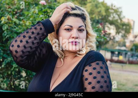 portrait young blonde latin woman from Argentina plus size model dressed in black, posing outdoors, looking at the camera. Stock Photo