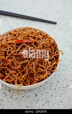 closeup of a palte with some chicken yakisoba noodles and a pair of black chopsticks, placed on a white mottled stone surface Stock Photo