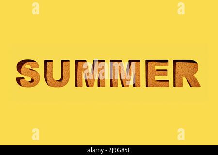 the word summer cut out on a yellow paper, and some sand in the background seen through the cutout letters Stock Photo