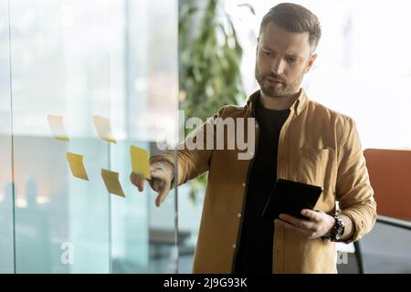 Businessman Sticking Notes On Glass Wall Holding Tablet In Office Stock Photo