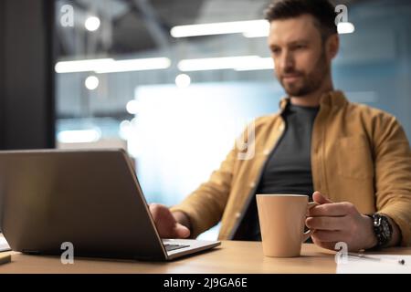 Businessman Using Laptop Drinking Coffee Working Online In Office Stock Photo
