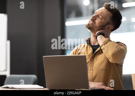 Businessman Touching Neck Suffering From Pain Using Laptop In Office Stock Photo