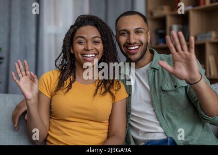 Joyful african american spouses waving hands and smiling to camera, talking online via video call, sitting at home Stock Photo