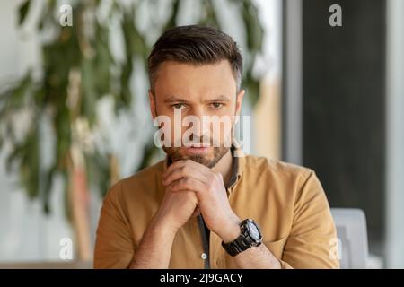 Serious Businessman Looking At Camera Sitting At Workplace In Office Stock Photo